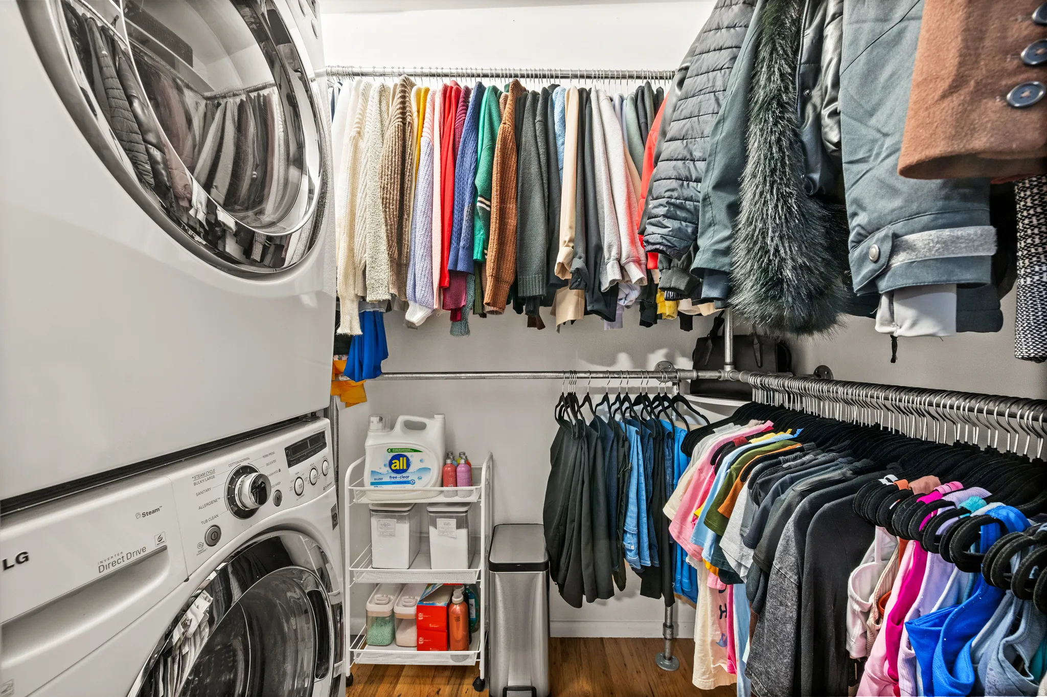 Laundry and closet area featuring stacked washer and dryer units, multiple clothing rods for organization, and wood-finish flooring