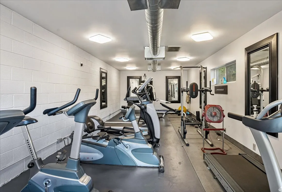 Dedicated fitness space featuring rubber flooring, exposed ductwork, wall-mounted mirrors, recessed lighting, and a horizontal window