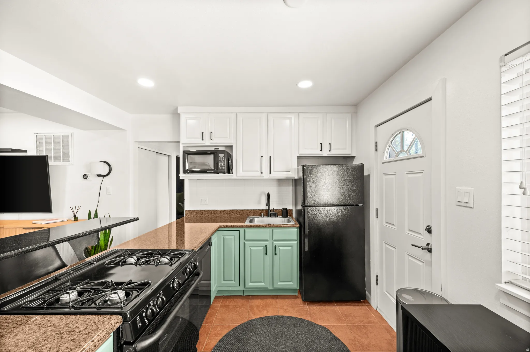 Compact kitchen featuring white upper cabinetry, mint green base cabinetry, and a black appliance suite