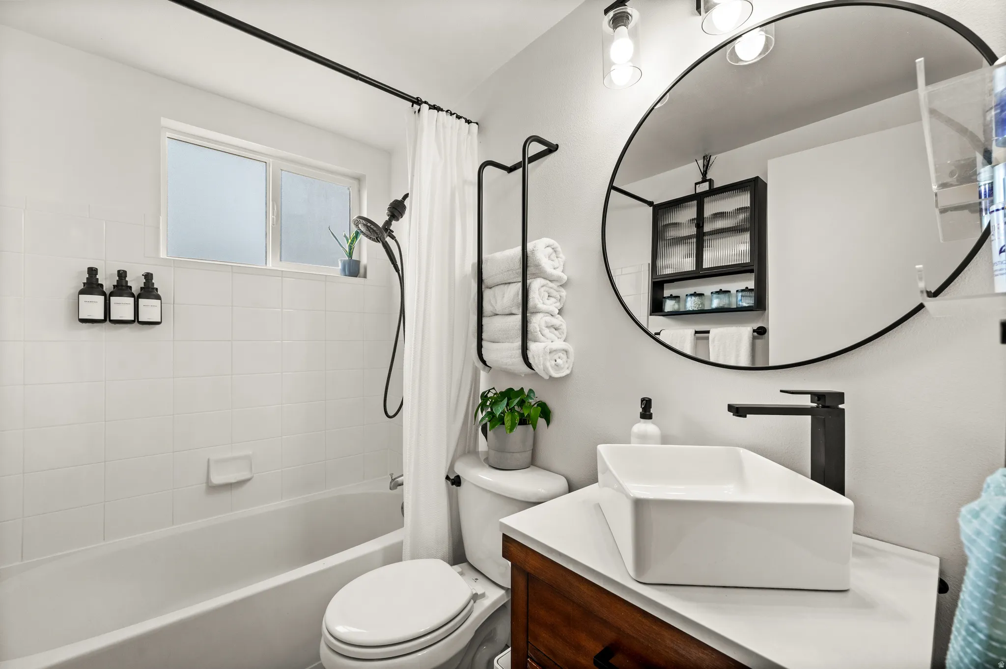 Modern bathroom featuring a rectangular vessel sink with a matte black faucet, a large round mirror, and a wood-finish vanity