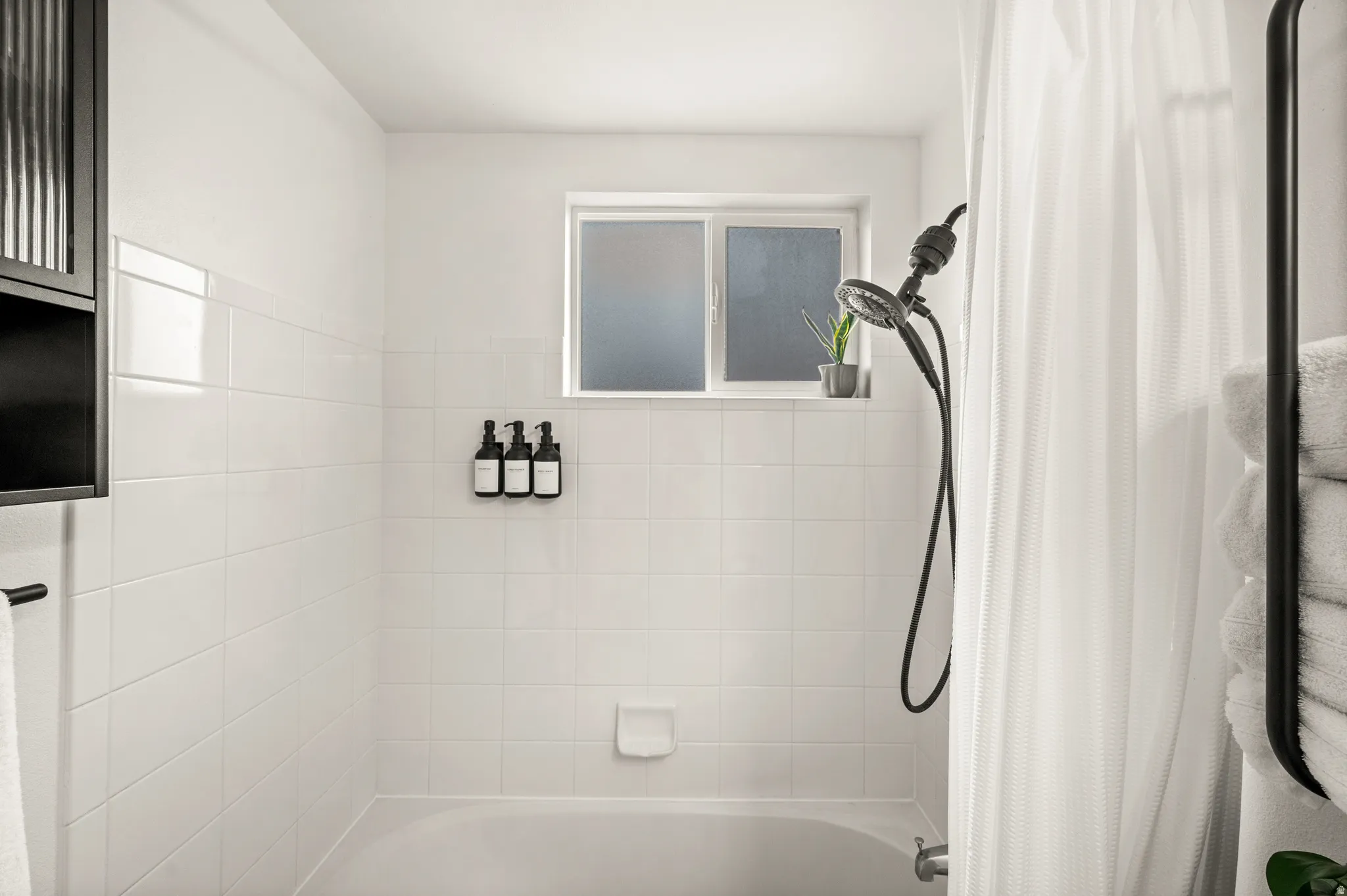 Shower-over-tub combination with white subway tile surround, matte black shower head and controls, and a privacy window
