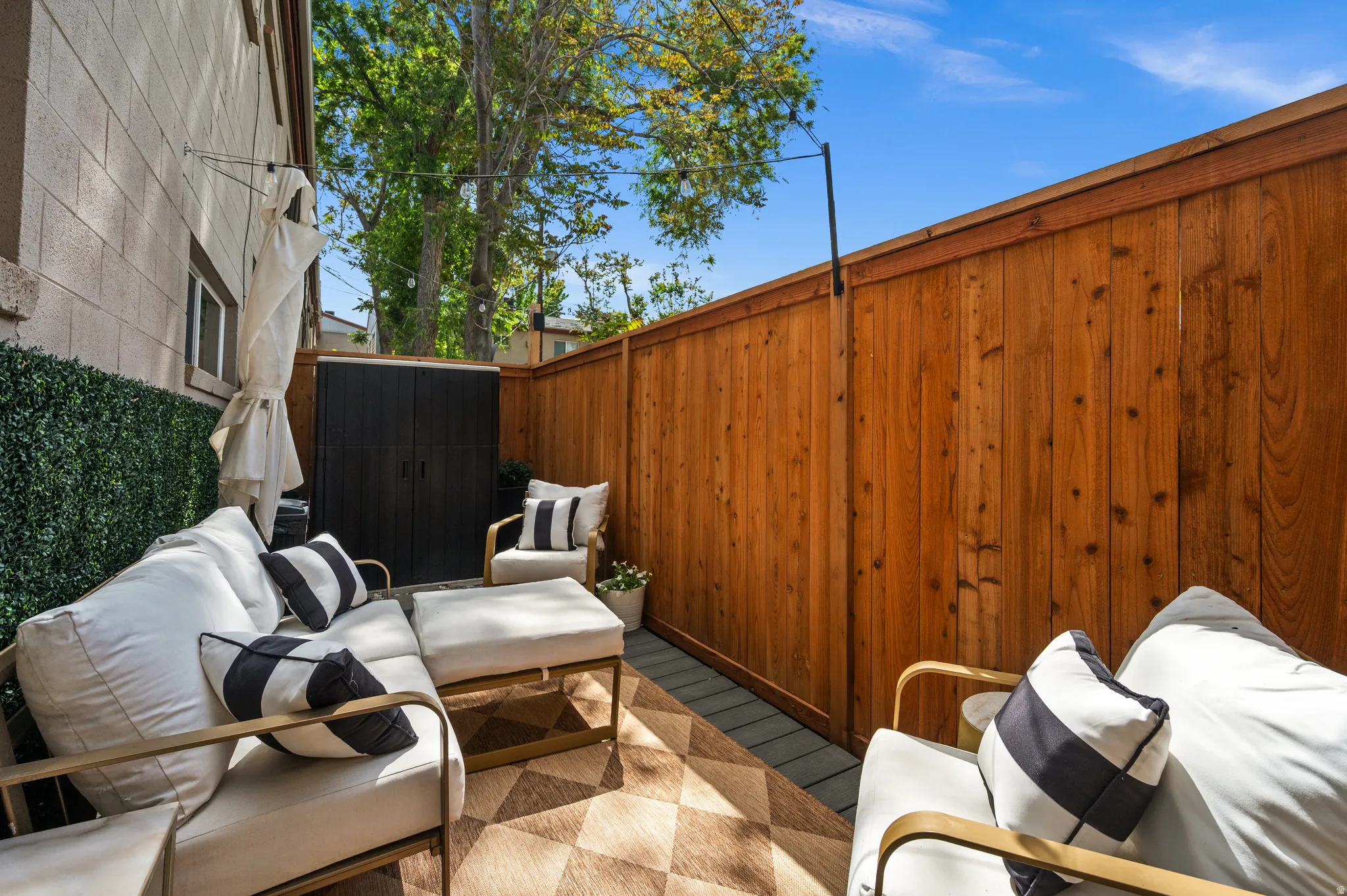 Private outdoor patio featuring a wood privacy fence, synthetic turf wall, concrete block wall exterior, and a contemporary storage shed