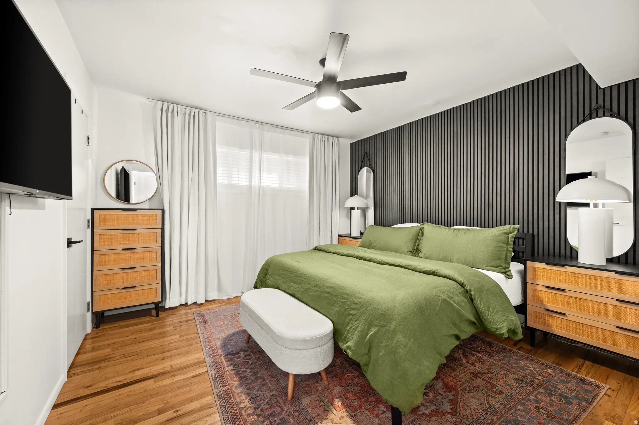 Bedroom featuring a slatted accent wall, wood-finish flooring, and a ceiling fan with integrated lighting