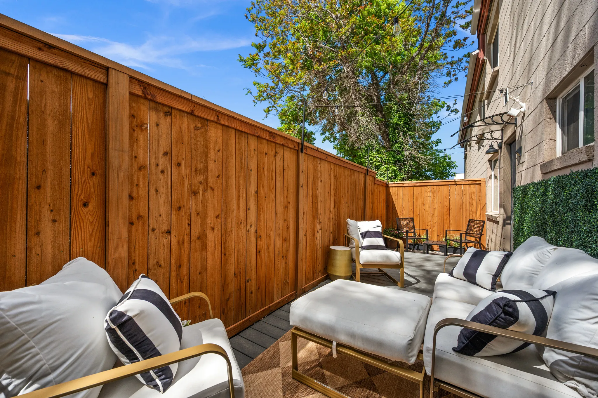 Outdoor patio area featuring composite decking, privacy fencing, a stucco exterior wall, and a decorative faux hedge panel