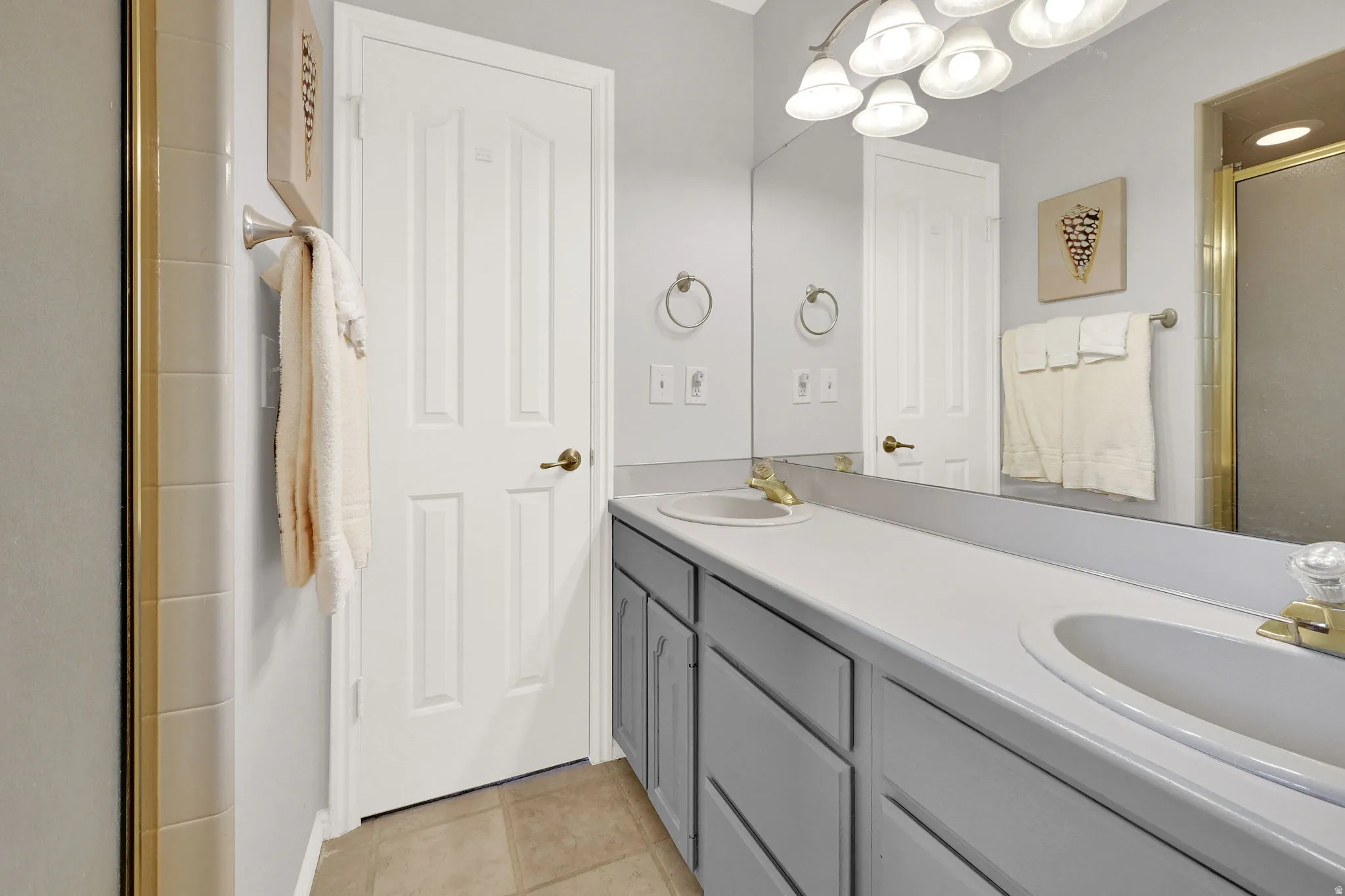 Primary bathroom with dual vanity with integrated sinks and gray cabinetry, expansive wall-mounted mirror, and tile flooring