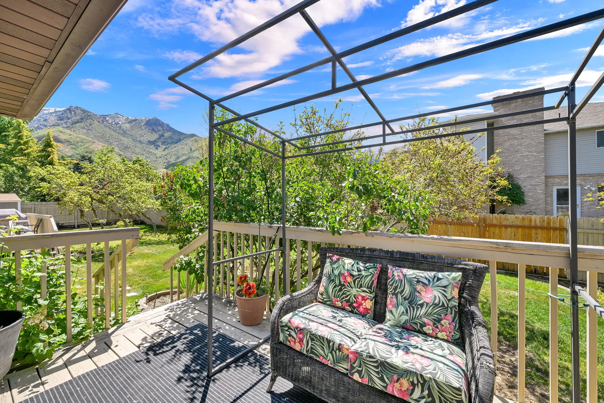 Outdoor deck with a metal pergola structure, wood railing, and a woven outdoor sofa off the primary bedroom