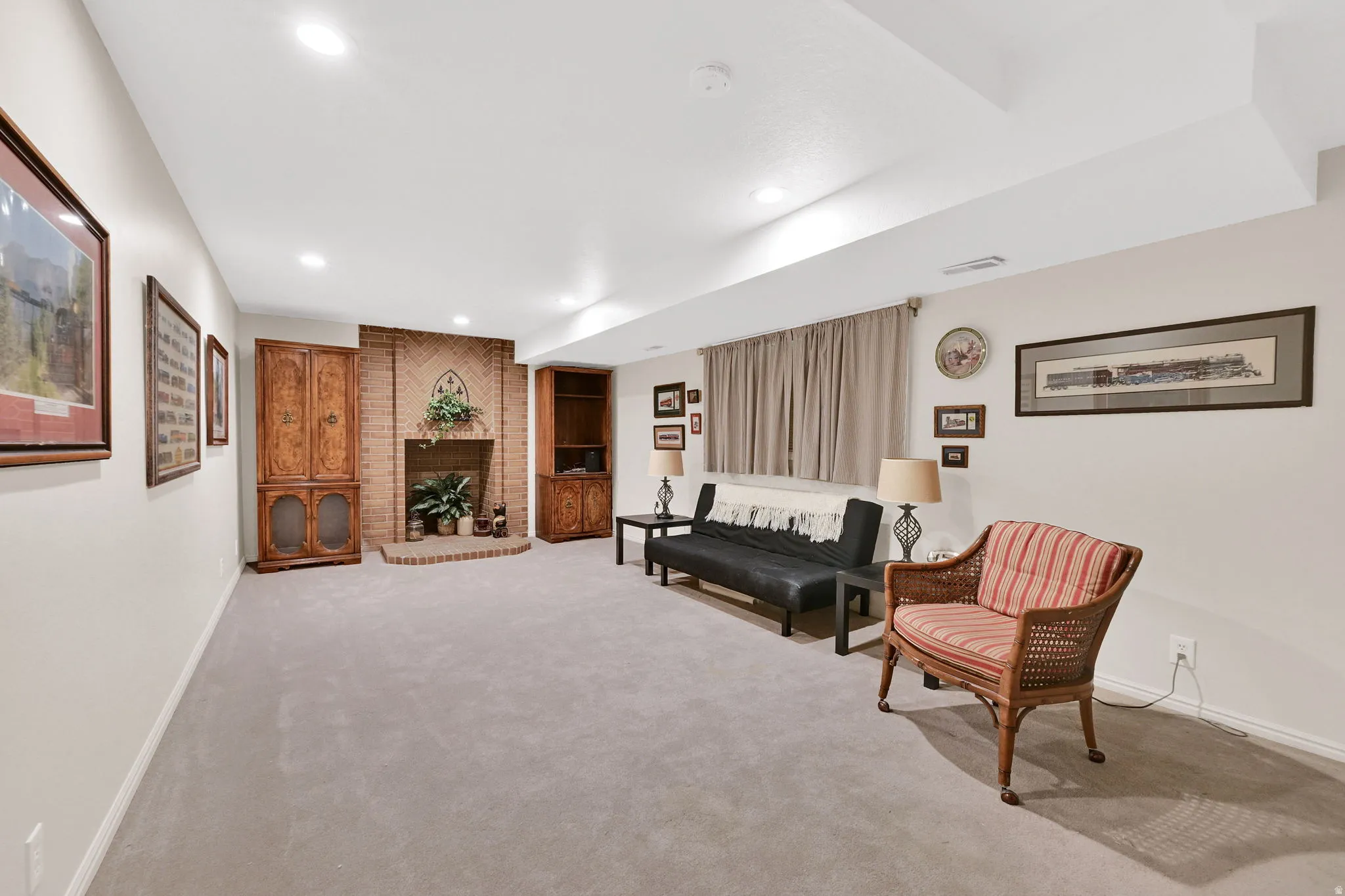 Spacious interior room featuring a brick fireplace area with a raised hearth, recessed lighting, and light-toned wall-to-wall carpeting