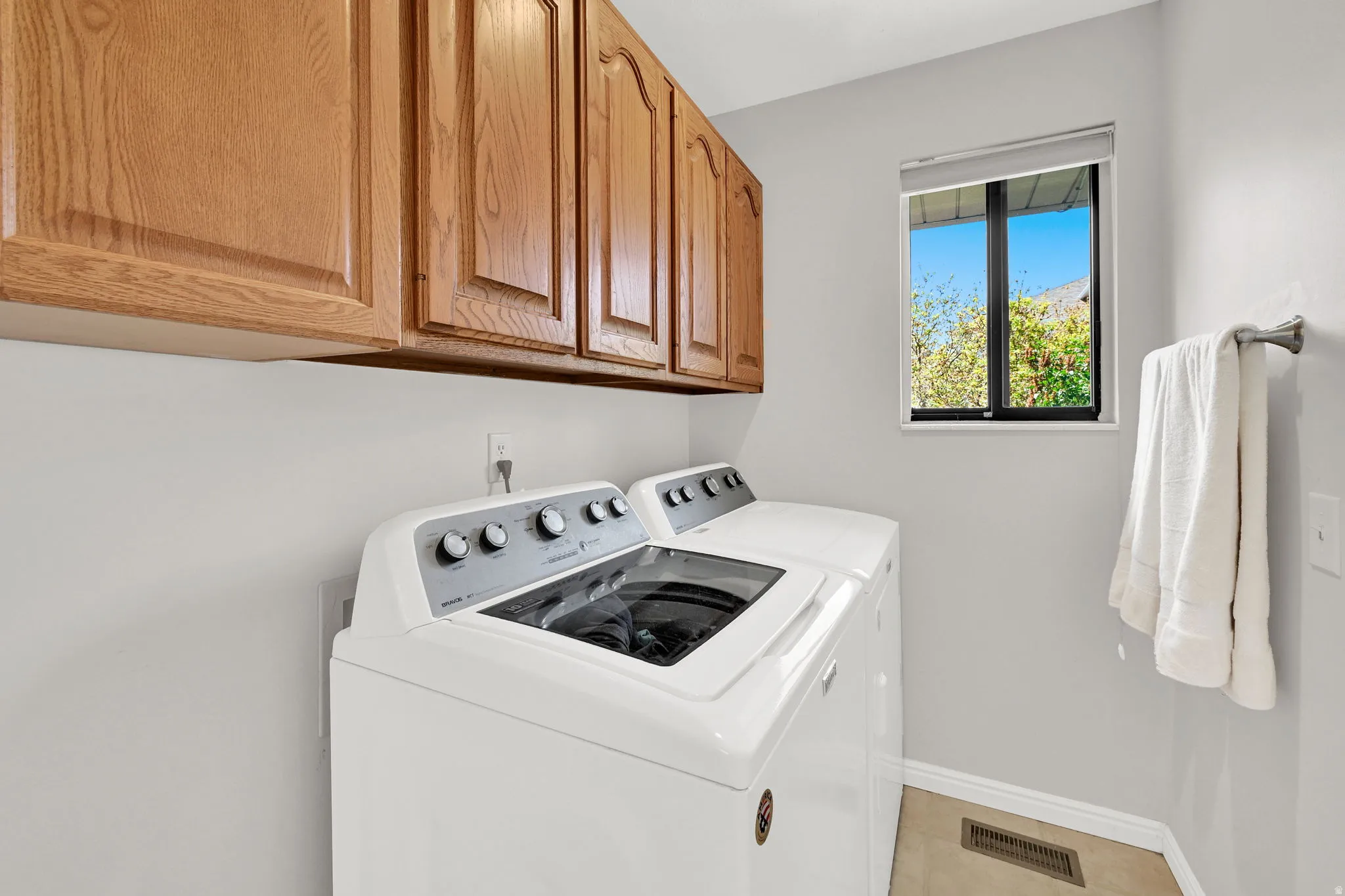 Laundry area with overhead wood cabinetry, a window, and a towel bar