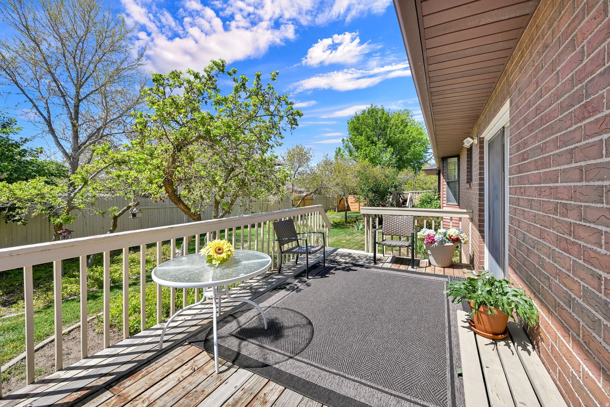 Expansive wood deck with white railings, featuring a brick exterior wall and a mature treed yard