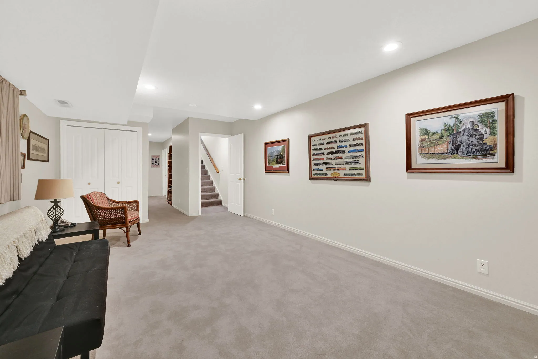 Spacious room featuring light gray carpeting, recessed ceiling lighting, a staircase with wood handrails, and bi-fold closet doors