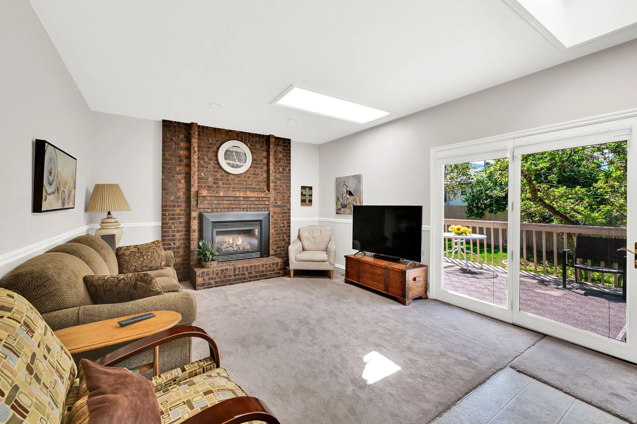 Living area featuring a brick fireplace surround with an insert, two skylights, and sliding glass doors opening to a wood deck and patio