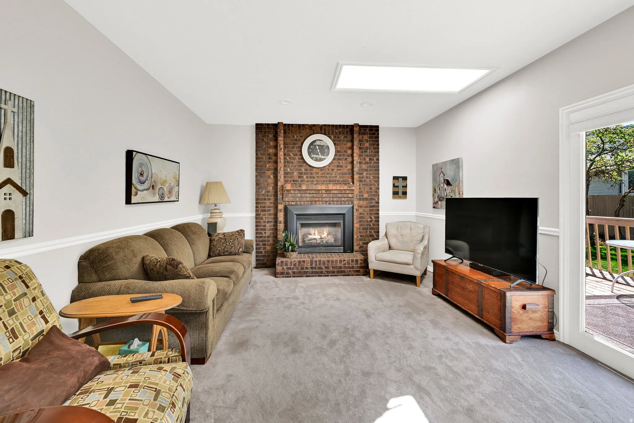 Living room featuring a prominent brick fireplace with a firebox, a rectangular ceiling skylight, and light gray wall paint