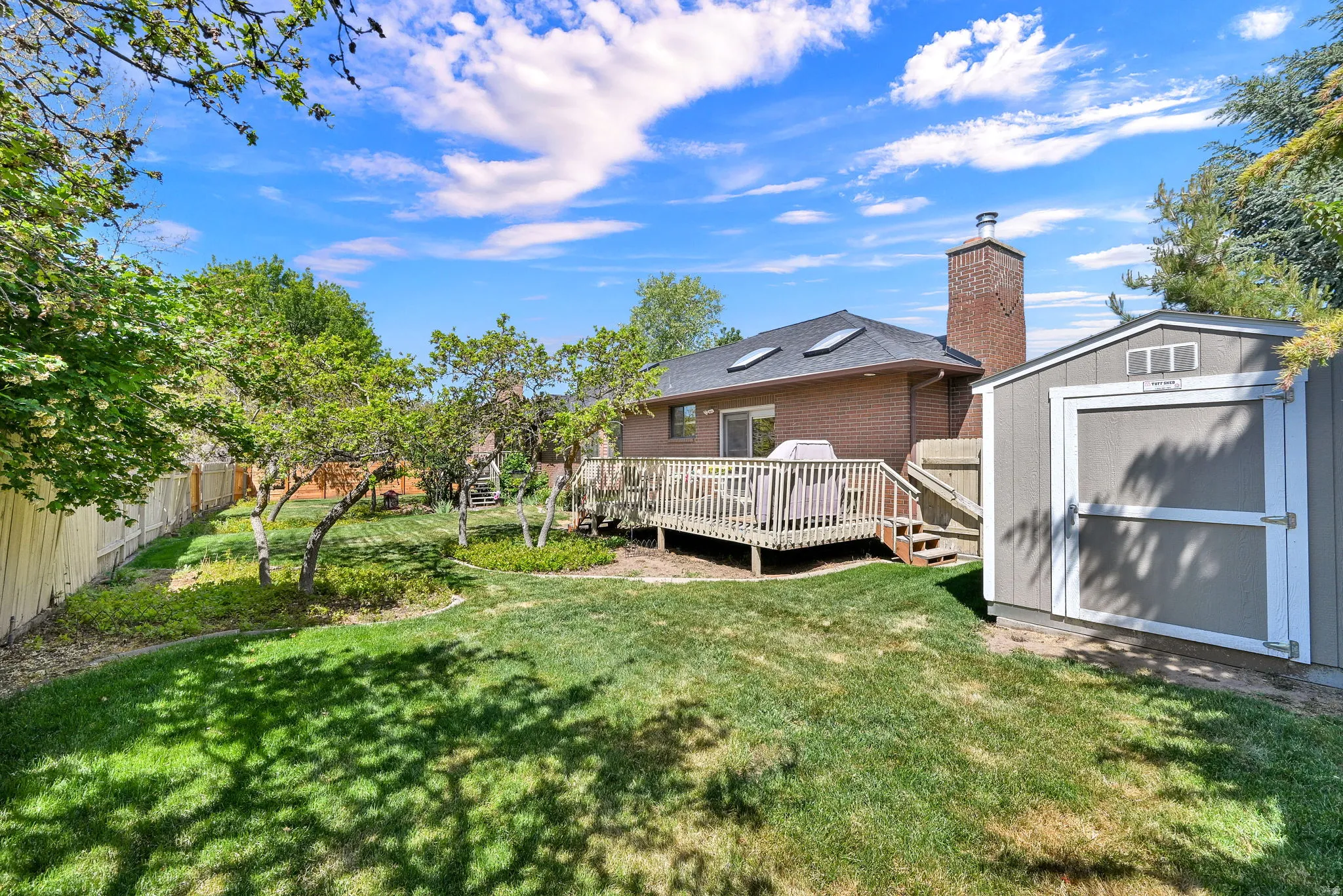 Expansive backyard featuring a manicured lawn, established trees, and a spacious wood deck and storage 8x10 shed