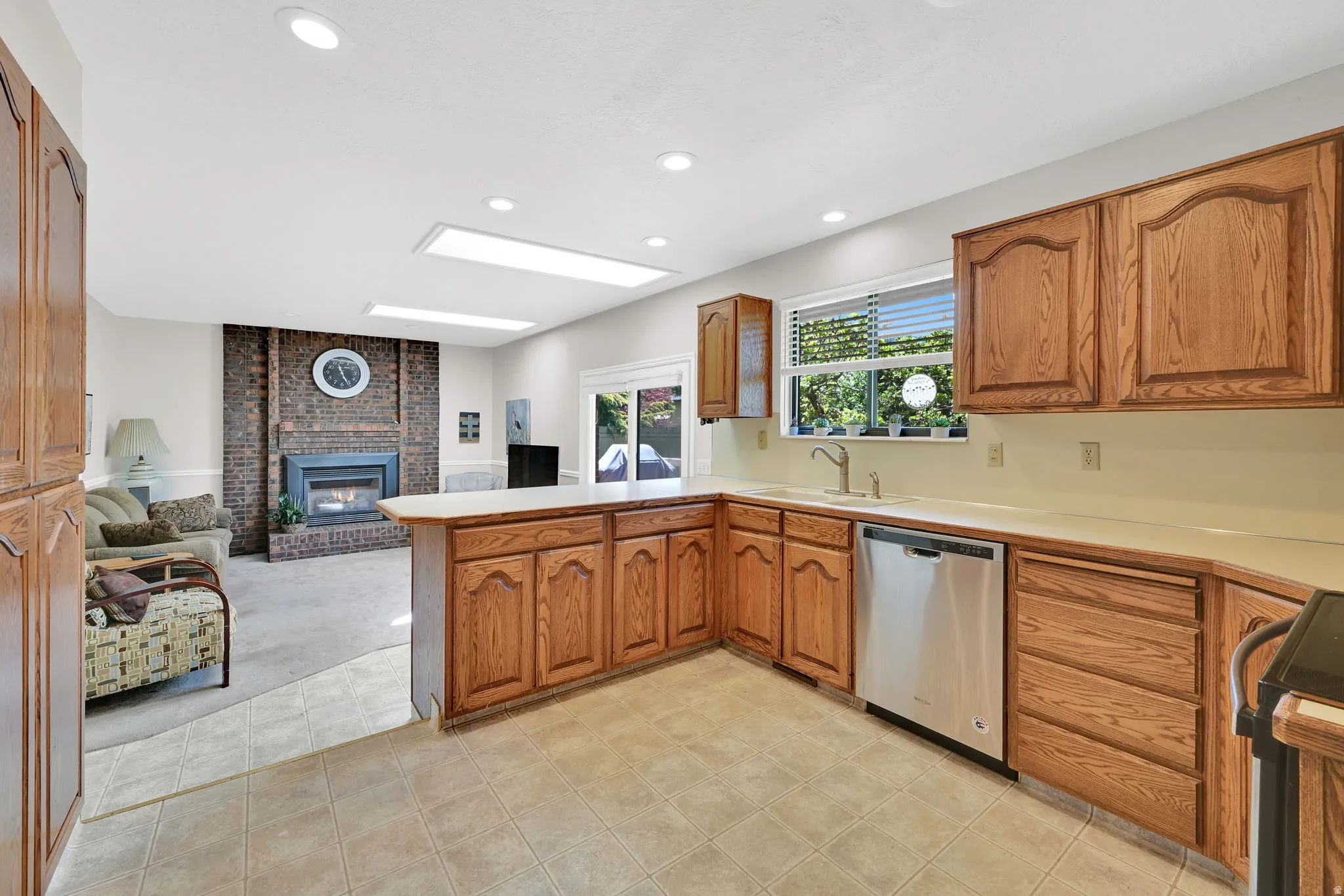 Kitchen featuring wood cabinetry, light-toned countertops, a stainless steel dishwasher, and tile flooring