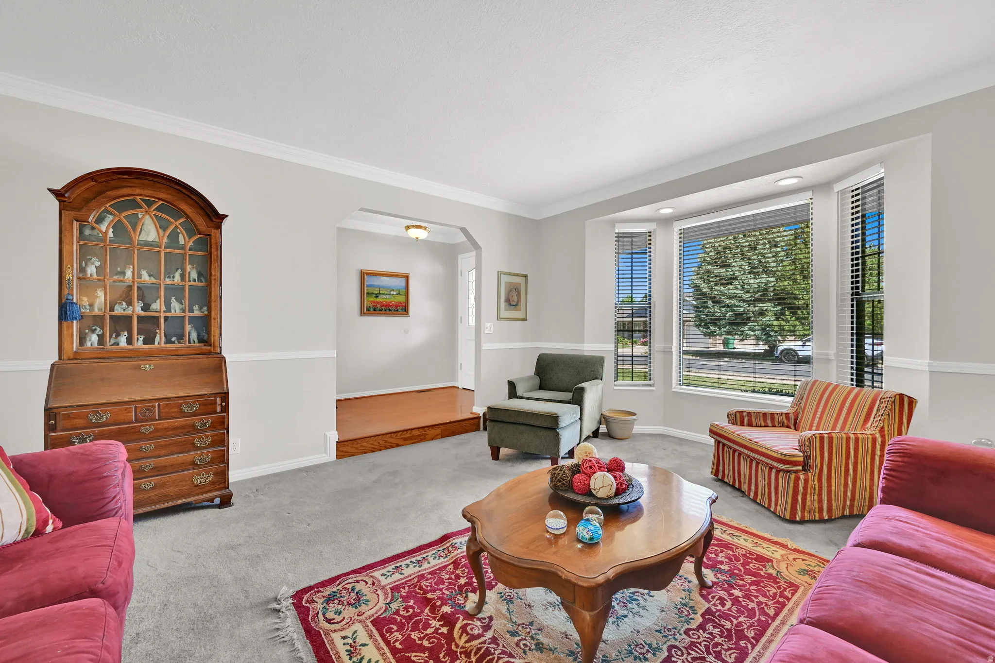 Living area featuring a bay window with blinds, light gray wall paint with white trim, and crown molding