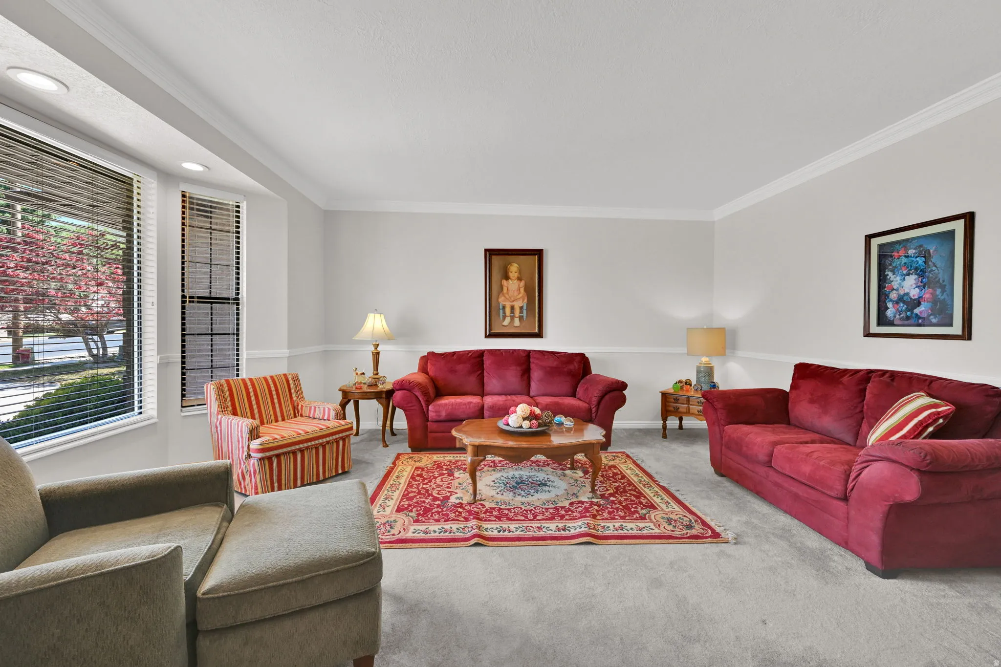 Carpeted living area featuring a bay window with blinds, crown molding, and wainscoting