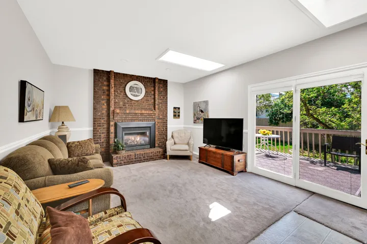 Living area featuring a brick fireplace surround with an insert, two skylights, and sliding glass doors opening to a wood deck and patio