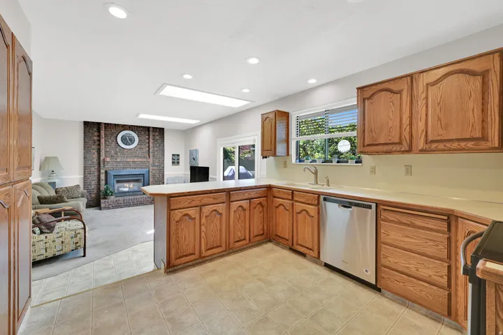 Kitchen featuring wood cabinetry, light-toned countertops, a stainless steel dishwasher, and tile flooring
