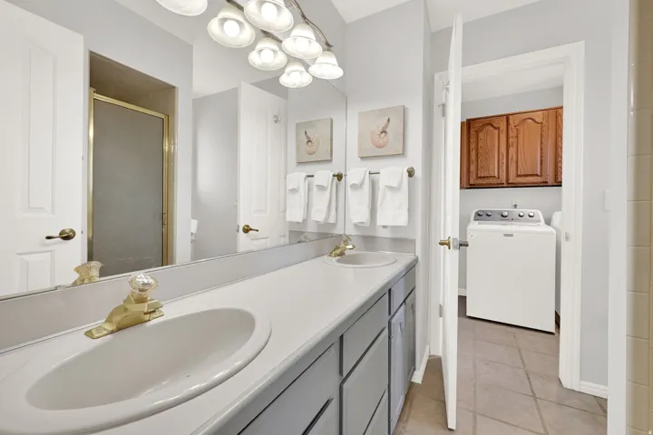 Primary bathroom with dual vanity featuring integrated sinks, a lengthy mirror, and overhead decorative lighting