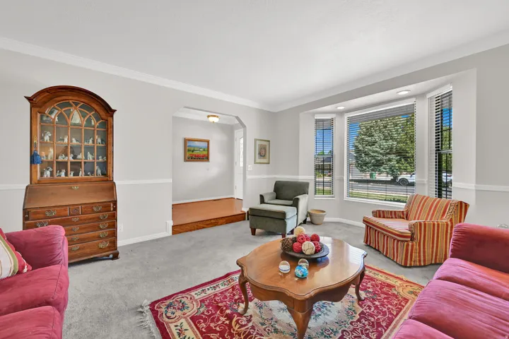 Living area featuring a bay window with blinds, light gray wall paint with white trim, and crown molding