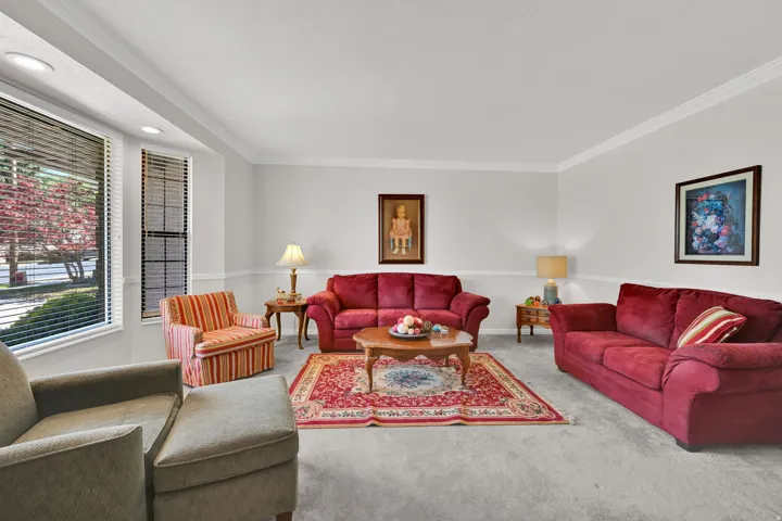 Carpeted living area featuring a bay window with blinds, crown molding, and wainscoting