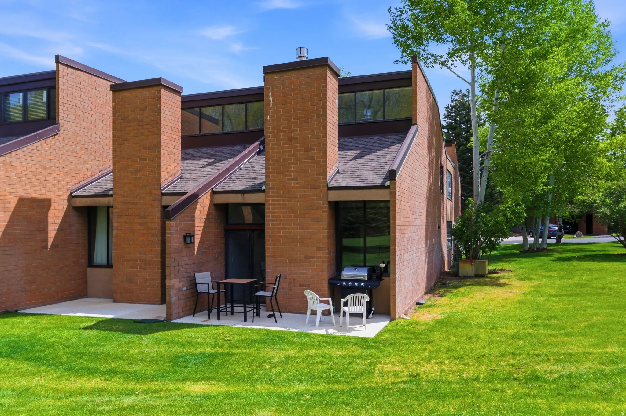 Brick exterior featuring a private patio, extensive green lawn, and mature trees