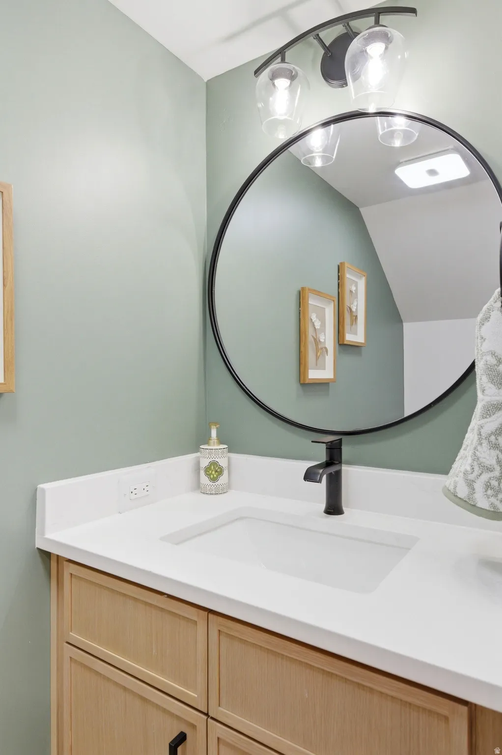 Bathroom vanity featuring light wood cabinetry, a white integrated sink, and a matte black faucet