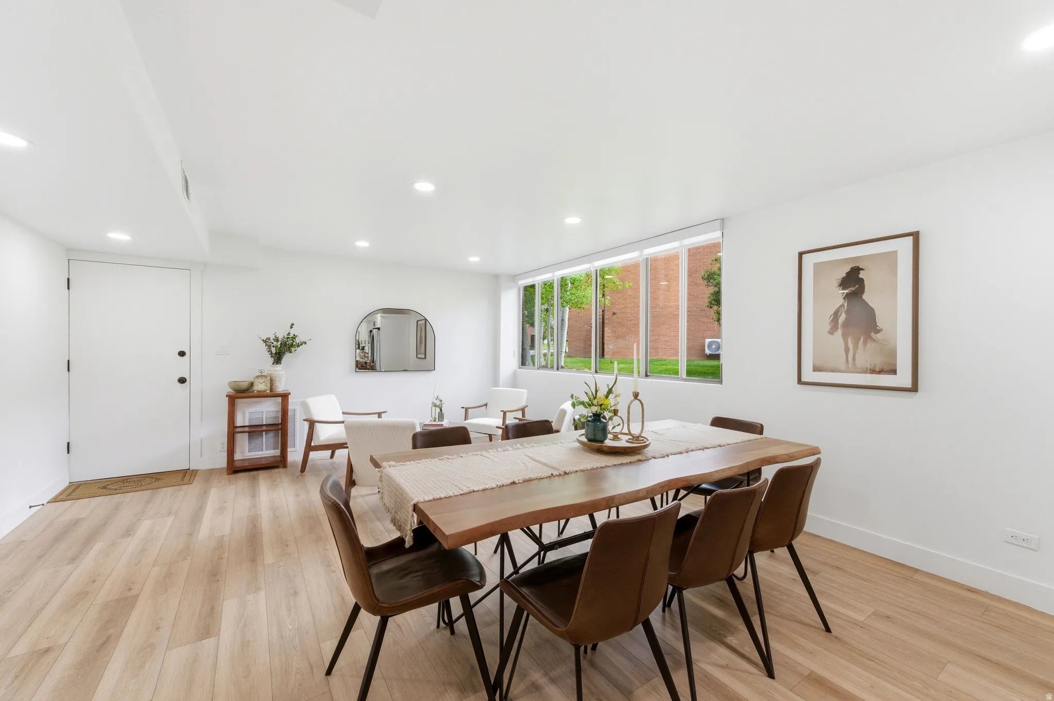 Open-concept living space with light wood-finish flooring, recessed lighting, and a prominent window spanning the wall