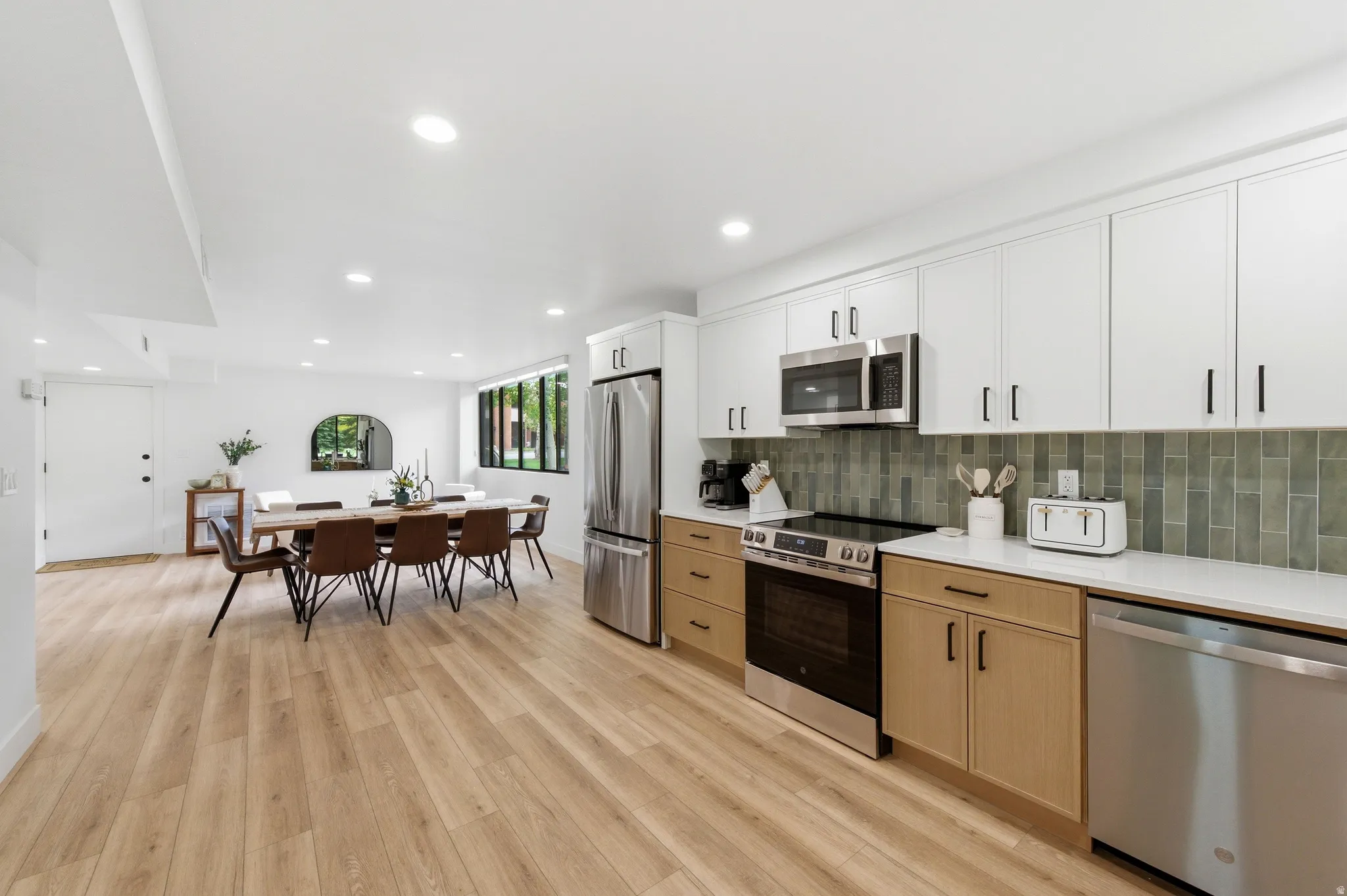 Contemporary kitchen featuring stainless steel appliances, two-tone cabinetry, white countertops, and a green tile backsplash