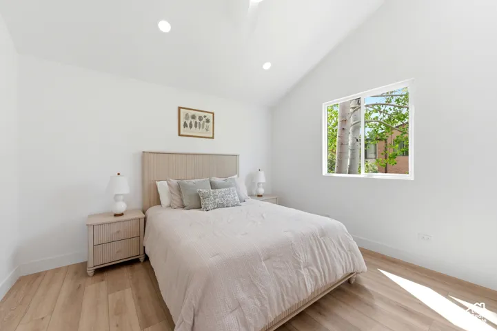 Vaulted ceiling with recessed lighting, wood-finish flooring, and a window providing natural light
