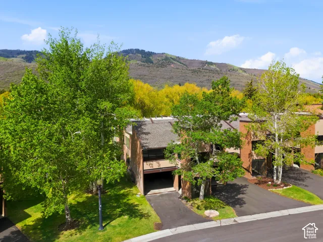 Mountain backdrop, paved driveway, mature trees, manicured lawn, multi-story structure