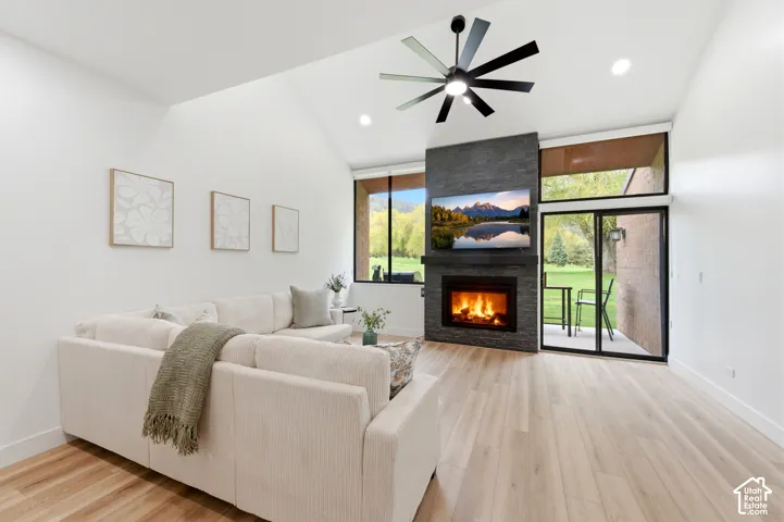 Vaulted ceiling, wood-finish flooring, stone-clad fireplace, built-in television mount, and glass sliding doors