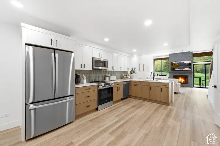 Open-concept kitchen with wood-finish flooring, two-tone cabinetry, stainless steel appliances, and a central island with a sink