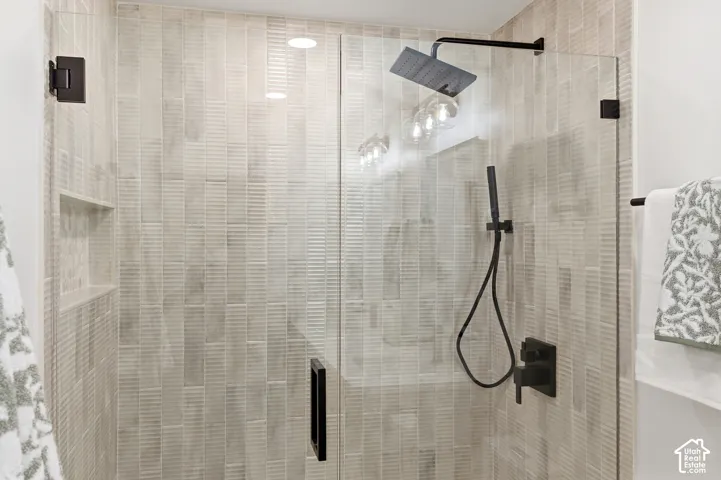 Glass-enclosed shower featuring textured wall tile, matte black fixtures, a built-in shower niche, and a rainfall showerhead