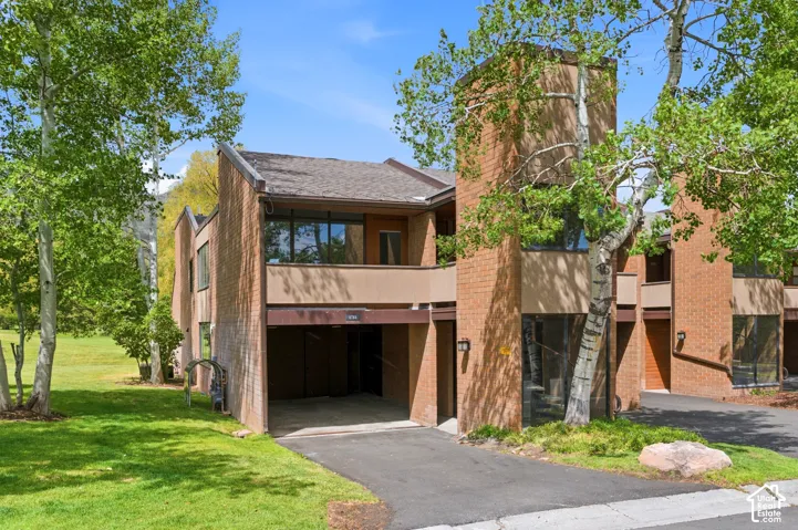 Brick exterior with multiple large windows, attached garage, private balcony, and surrounding mature trees