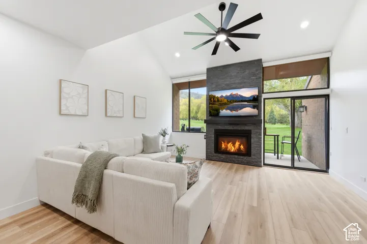 Vaulted ceiling with recessed lighting, wood-finish flooring, full-height stone fireplace, and a glass sliding door