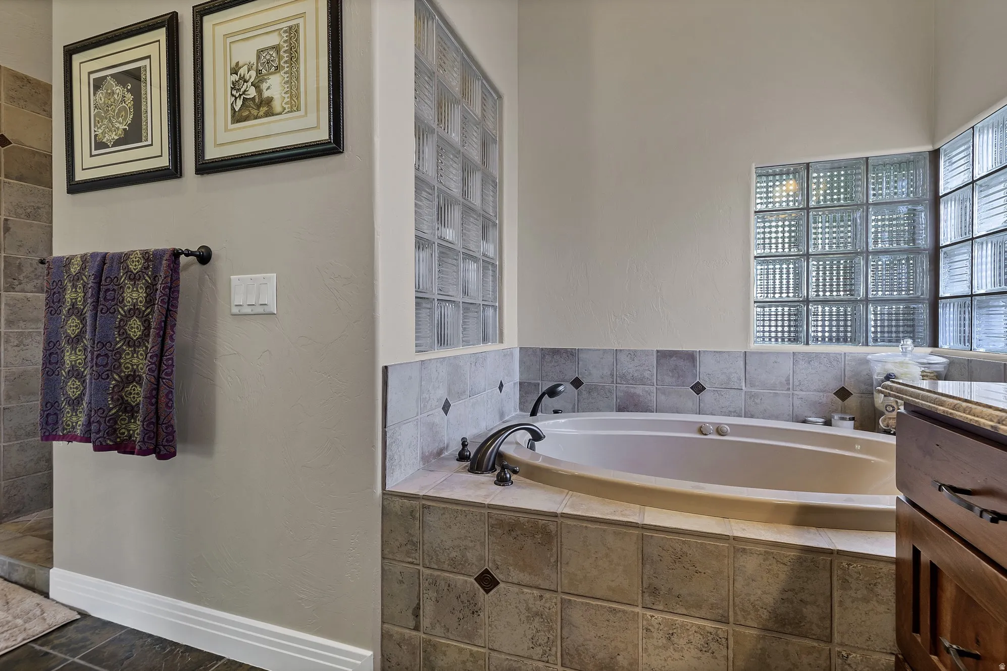 Soaking tub with bronze fixtures, surrounded by a tiled deck and glass block windows