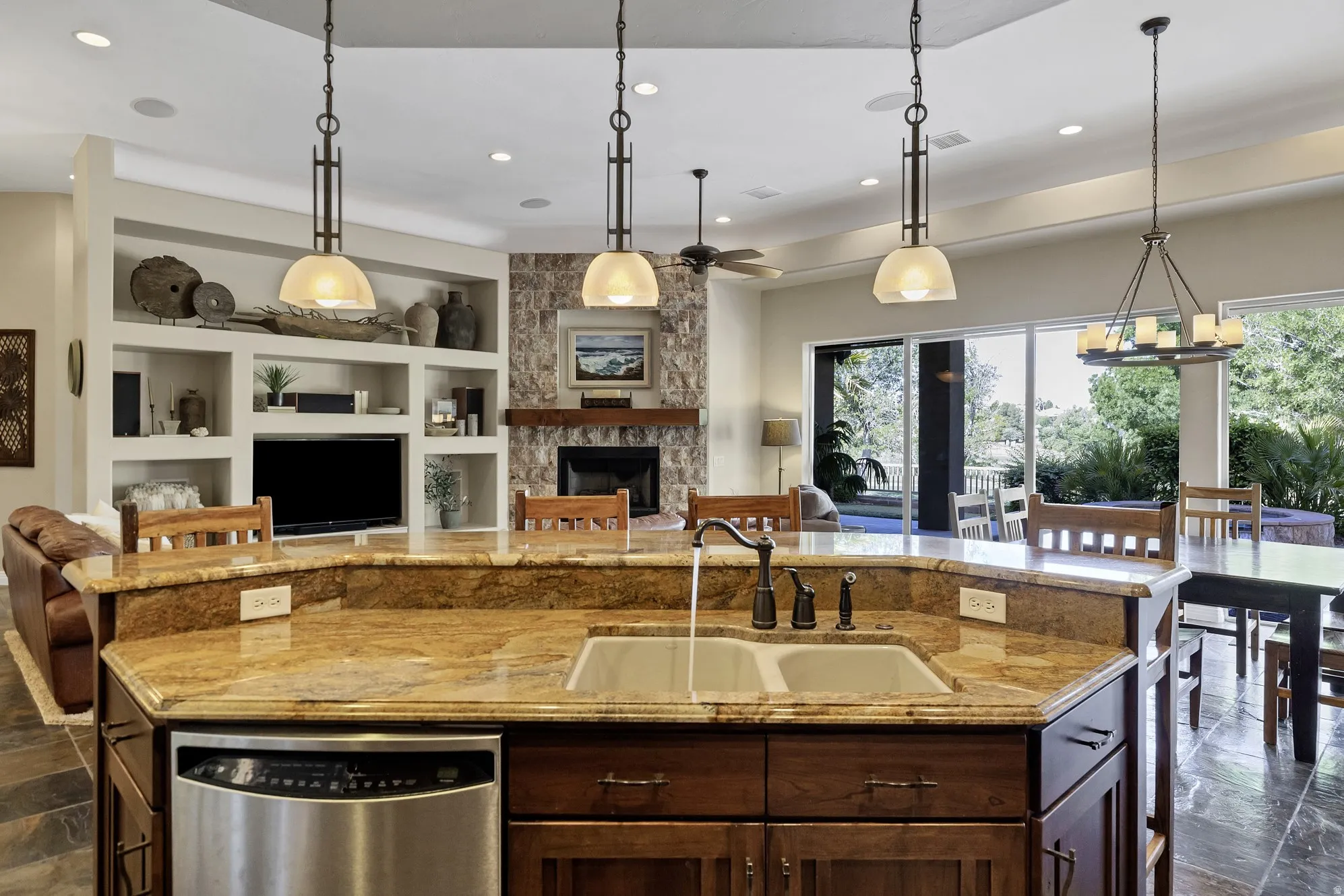 Kitchen island featuring a dual basin sink with a bronze-finish faucet, granite countertops, and integrated stainless steel dishwasher