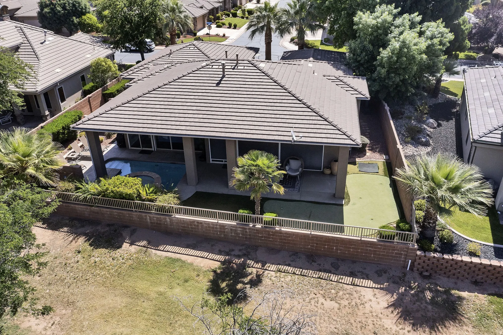 Rear exterior featuring a covered patio, integrated pool and spa, and an artificial turf putting green