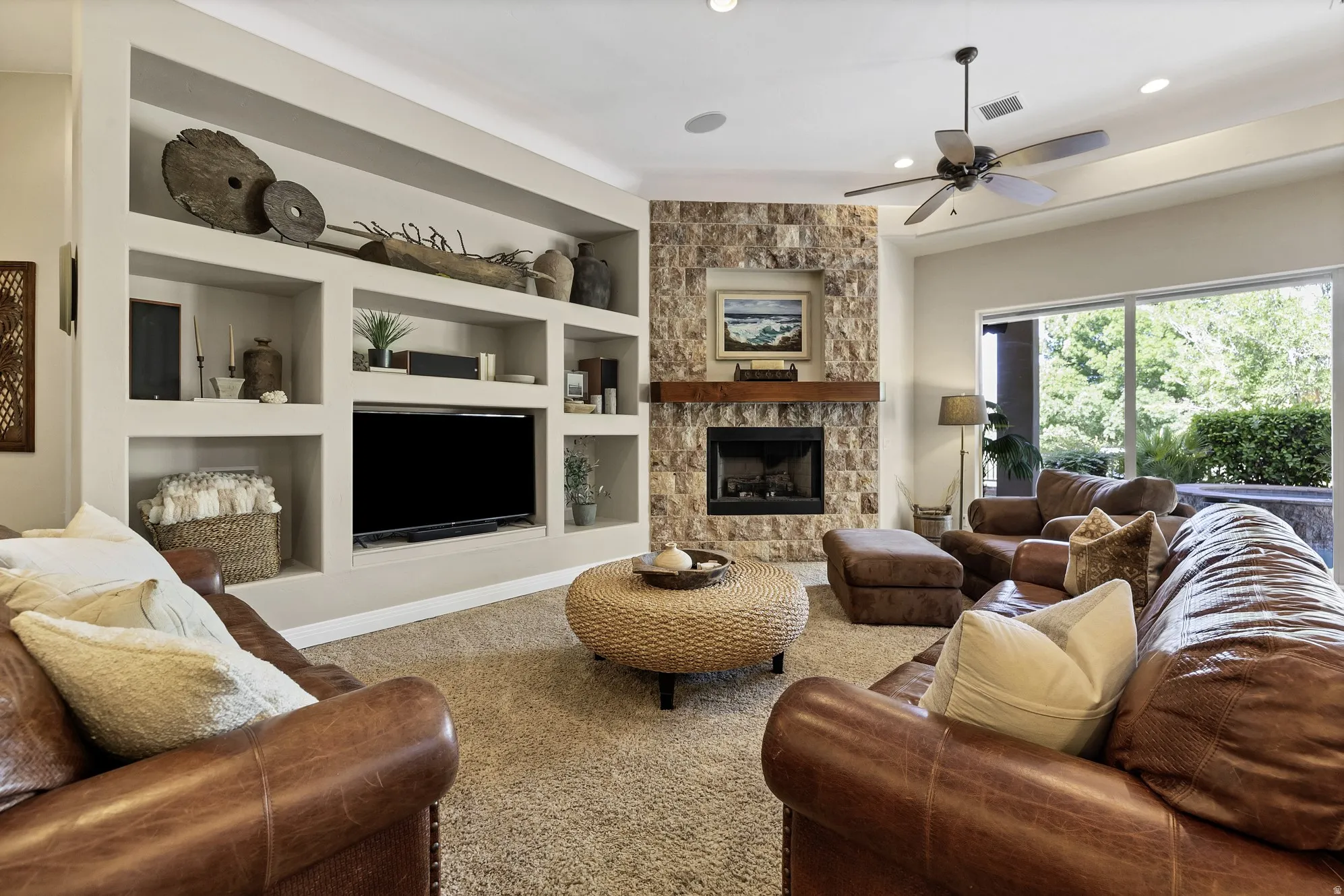 Living area featuring a stone-clad fireplace with a wood mantle, built-in shelving, recessed lighting, and a ceiling fan