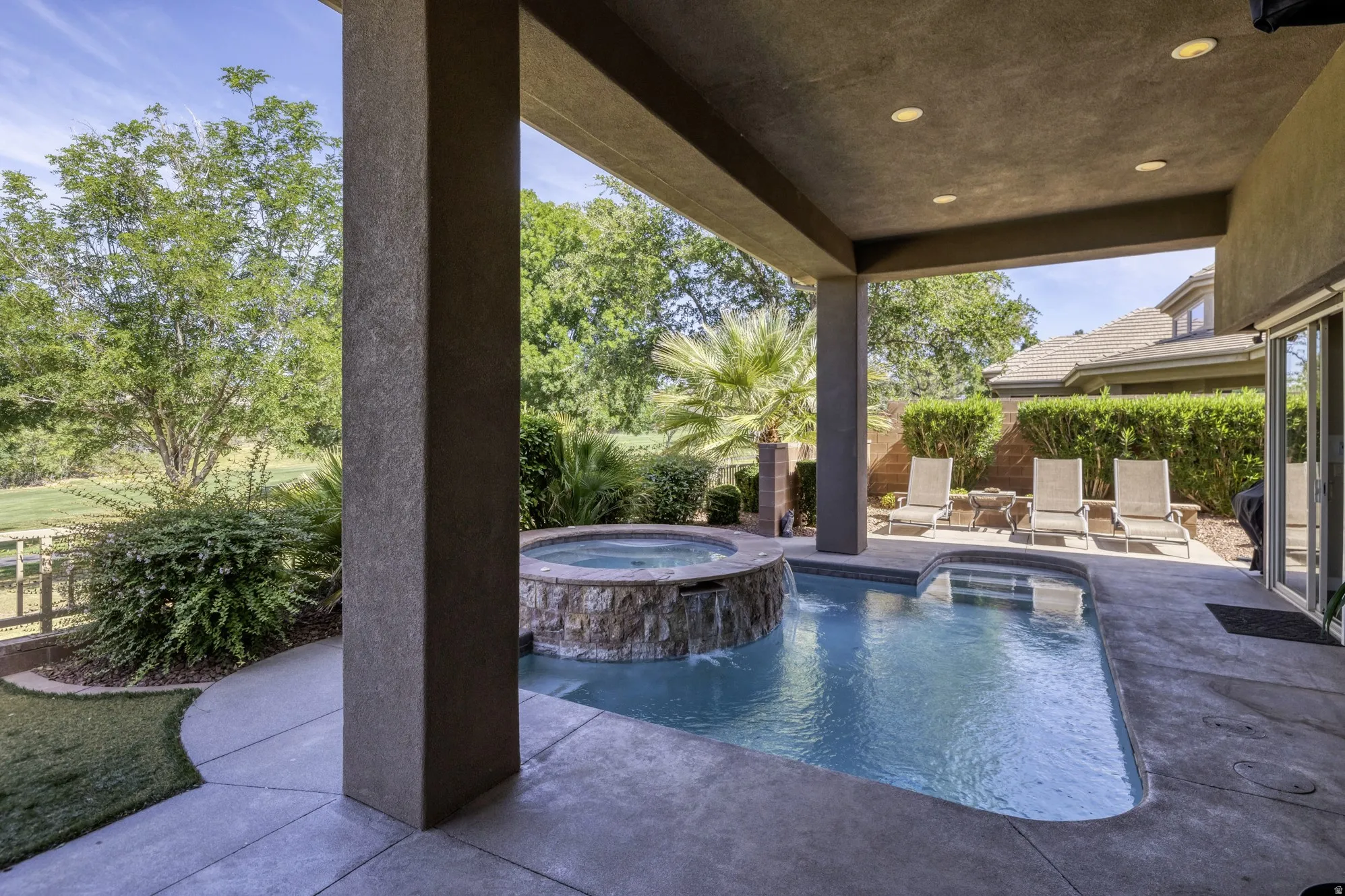 Covered patio featuring an integrated spa and swimming pool with a stone-clad waterfall
