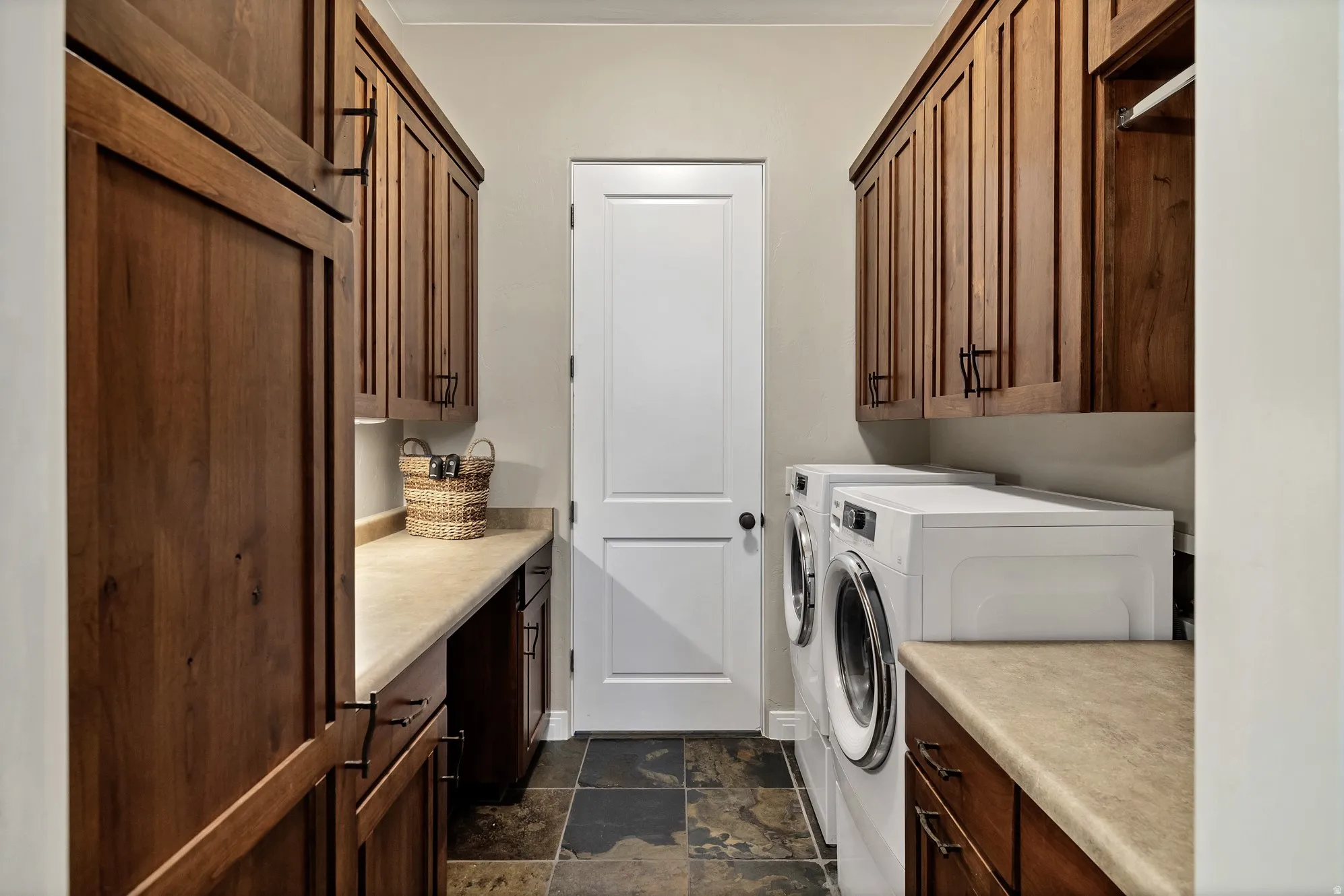 Dedicated laundry area featuring abundant wood cabinetry, integrated countertops, and slate-style floor tiling