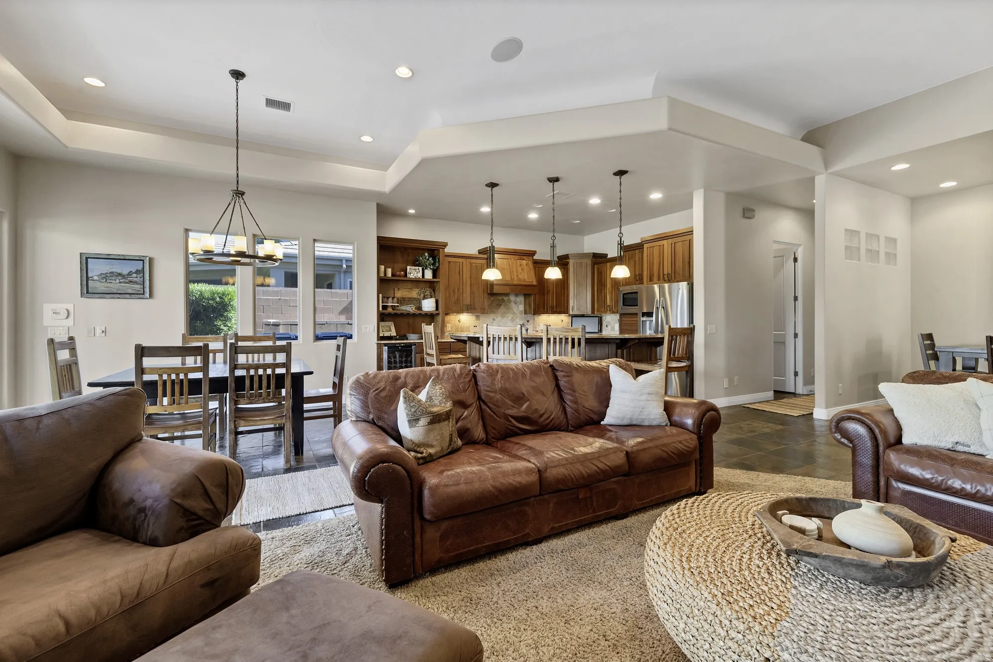 Open-concept living space featuring tray ceilings, recessed lighting, and a dining area with a modern linear chandelier
