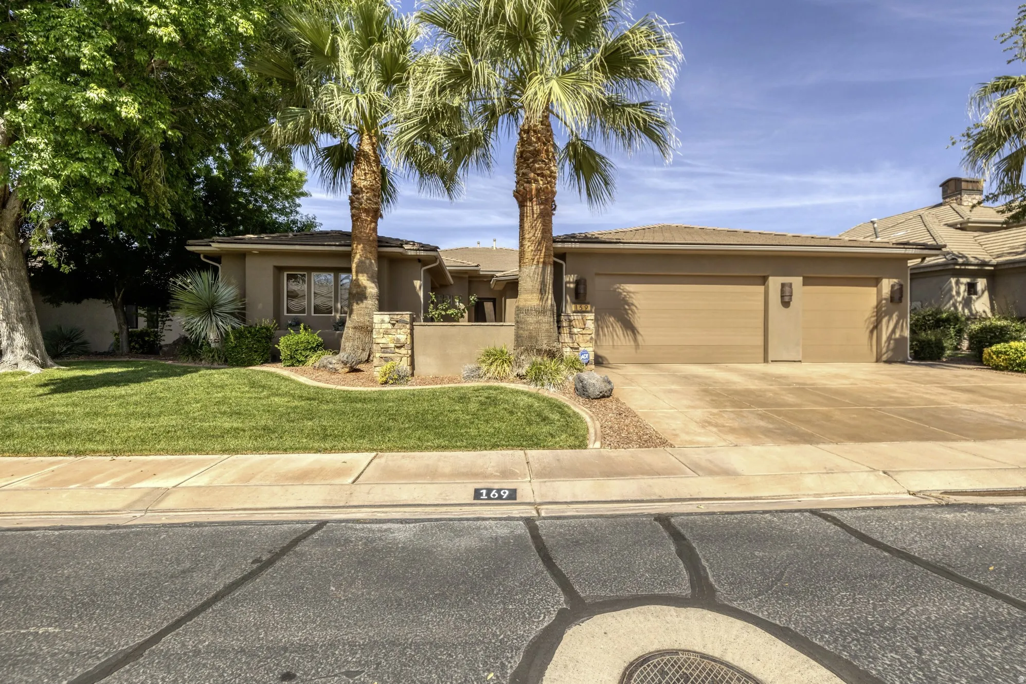 Desert-toned stucco residence featuring a two-car garage, mature palm trees, and manicured lawn