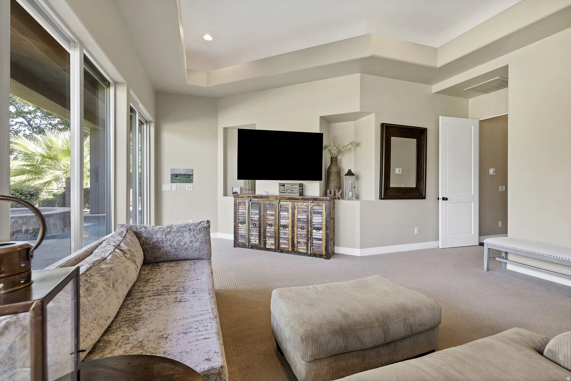 Spacious room featuring broad sliding glass doors, a recessed wall niche for media, a tray ceiling, recessed lighting, and neutral wall paint