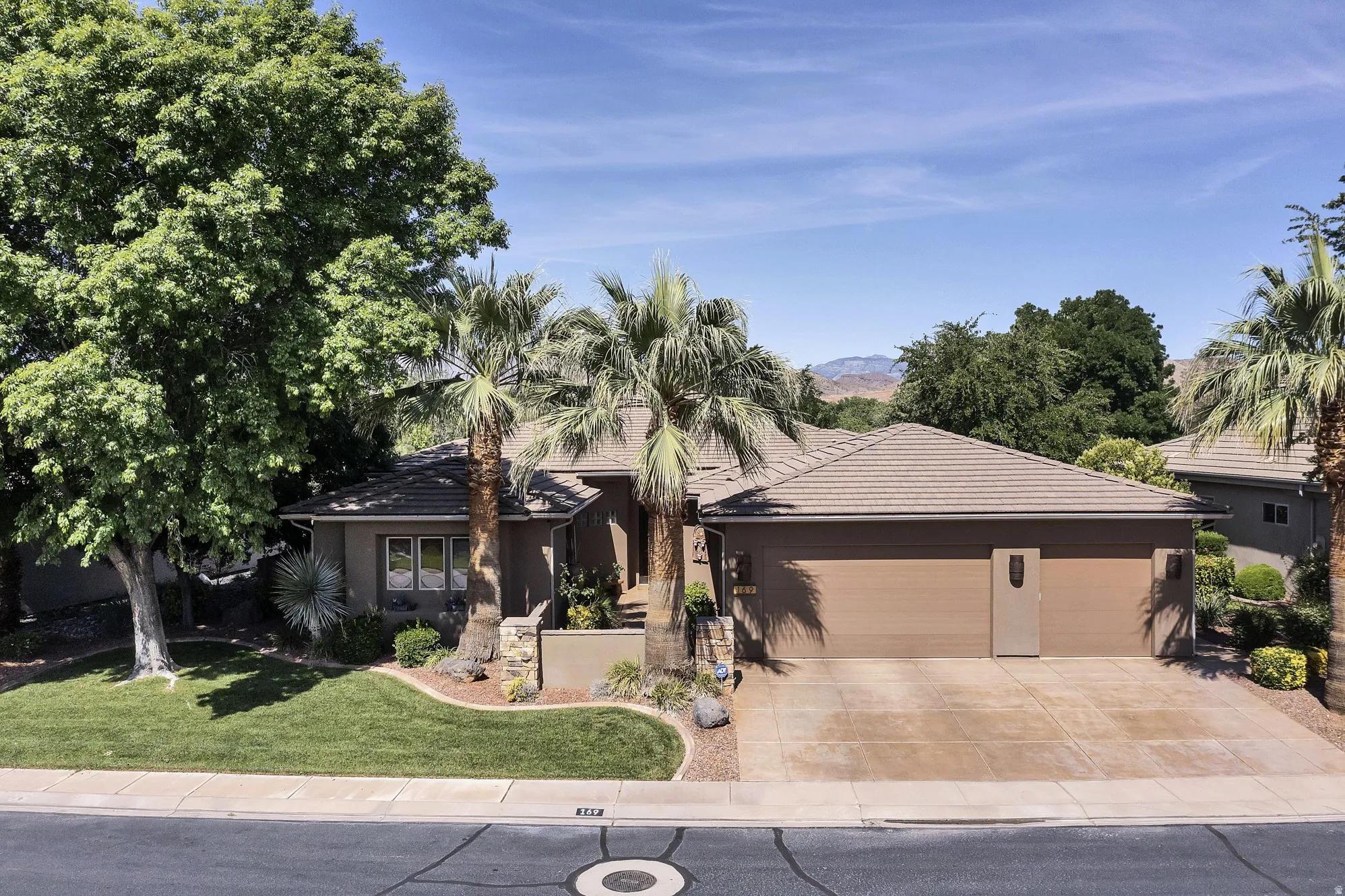 Single-story residence featuring a tile roof, an integrated two-car garage with a concrete driveway, and established desert landscaping with palm trees