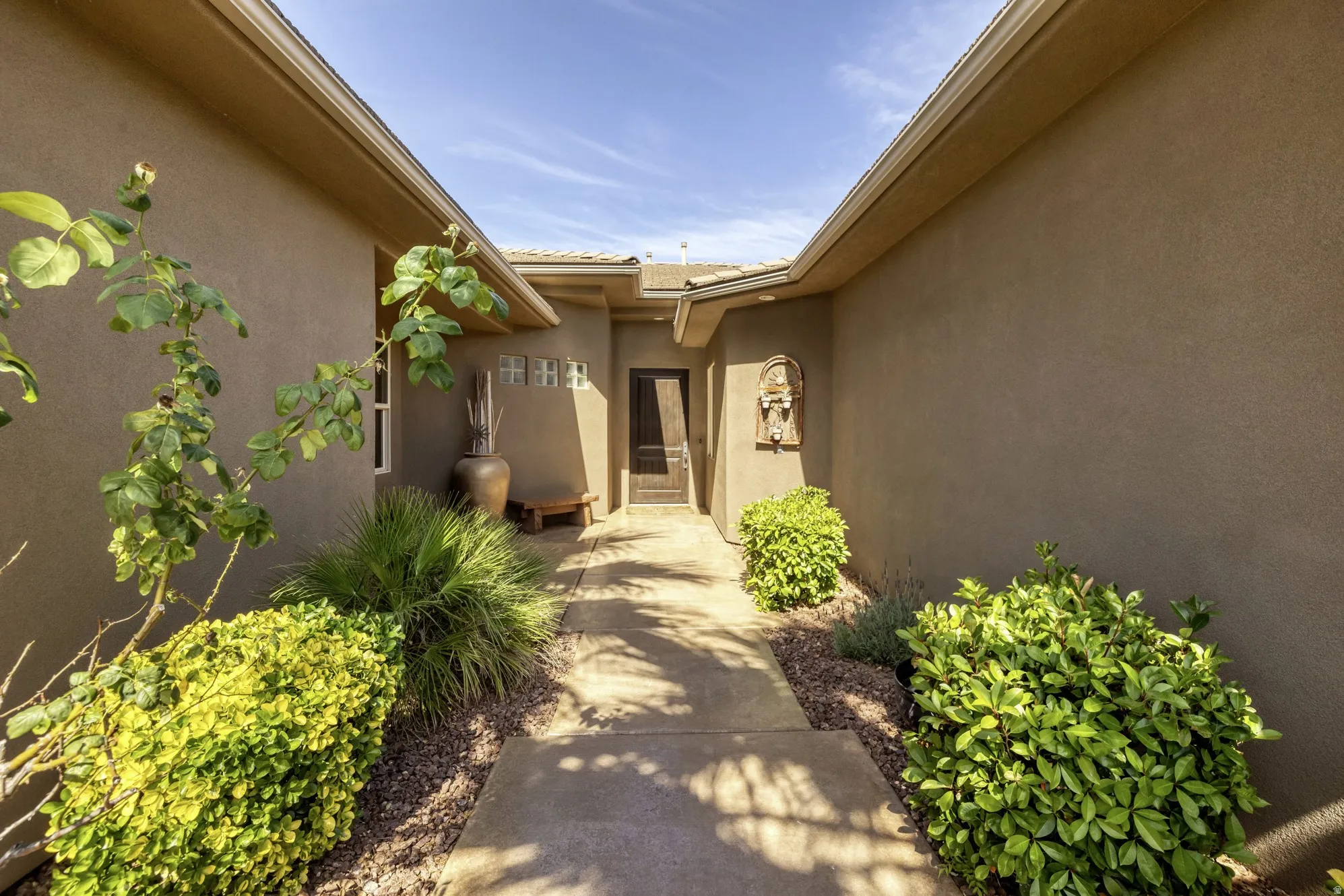 Stucco exterior featuring a covered entryway, concrete pathway, and Xeriscape landscaping with mature plantings