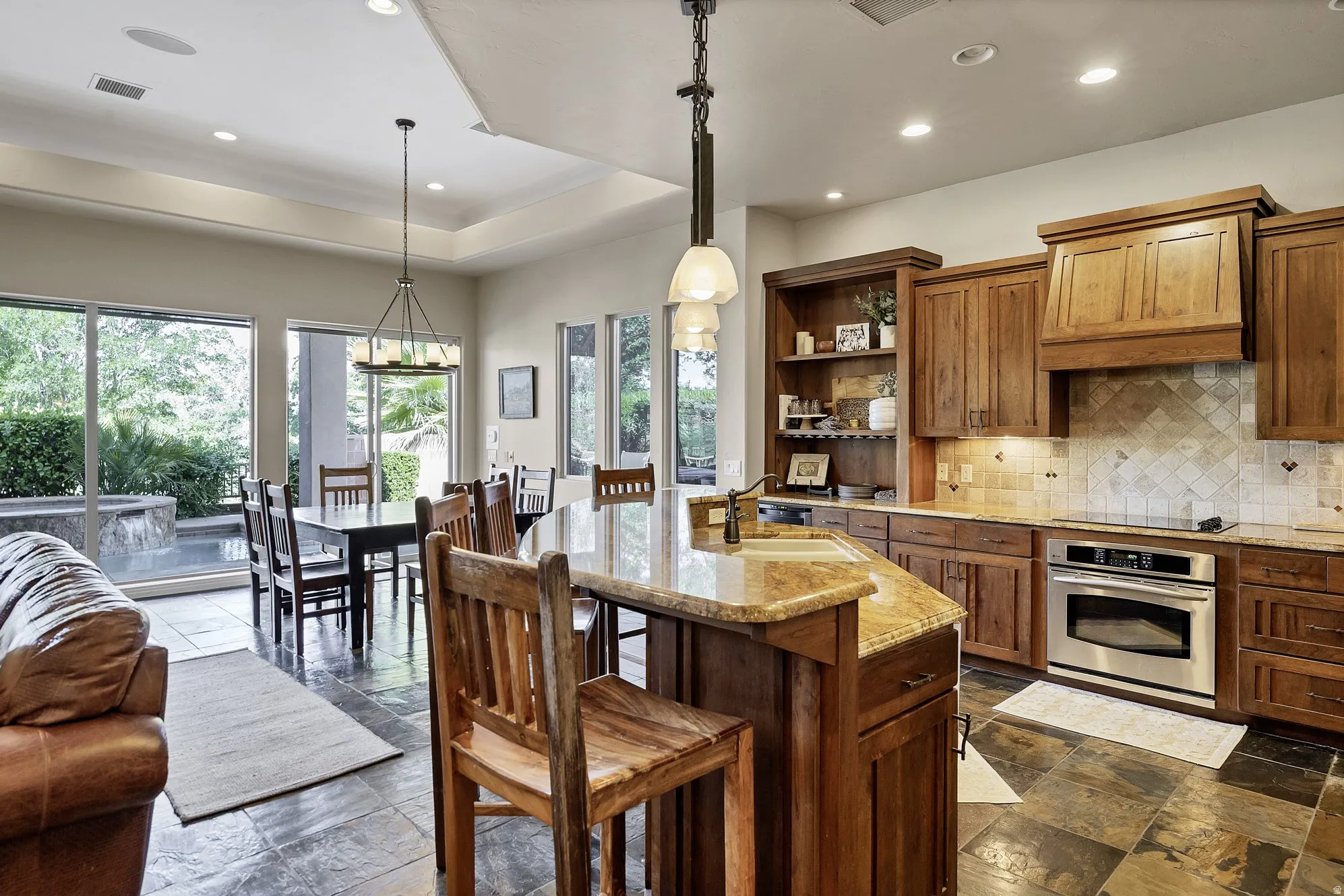 Open-concept kitchen and dining area featuring slate-finish flooring, warm wood cabinetry, a built-in oven, and a kitchen island with stone countertop
