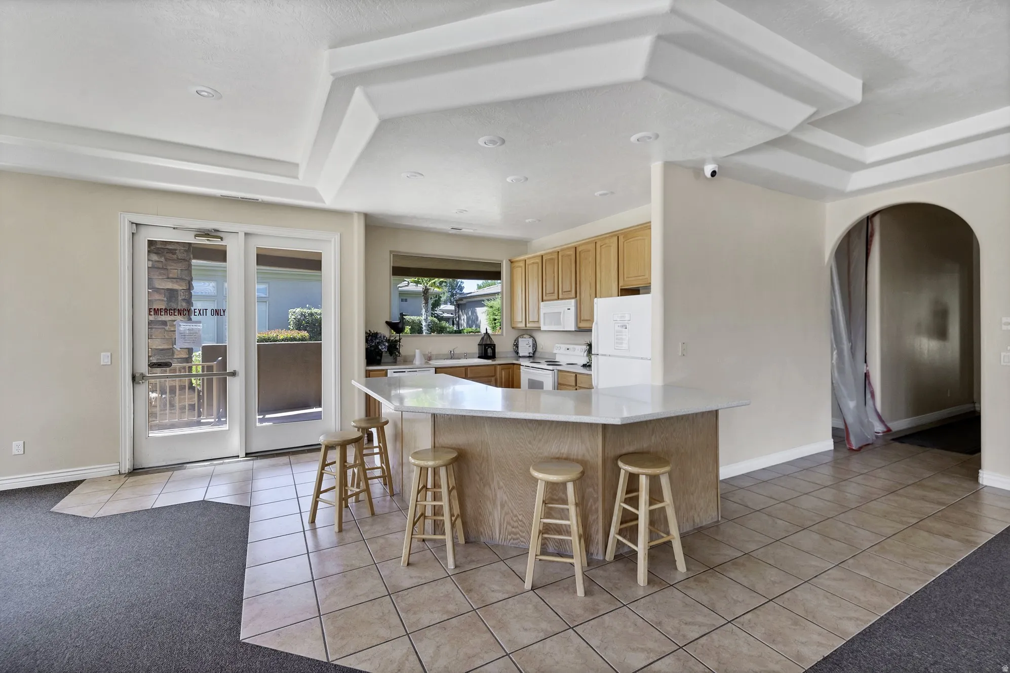 Open-concept common area featuring a kitchen with light wood cabinetry, a breakfast bar with a light-toned countertop, and recessed lighting