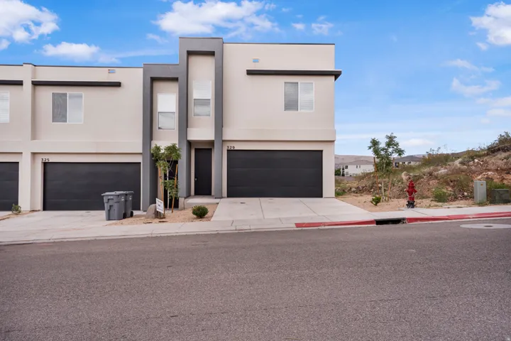 Modern architectural townhome featuring a neutral stucco exterior with dark trim accents, a single-car garage, and an entry door